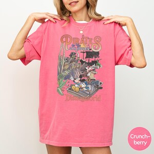 A woman wearing a pink t-shirt with a graphic of Disney characters and text related to the Pirates of the Caribbean ride at Disney World.