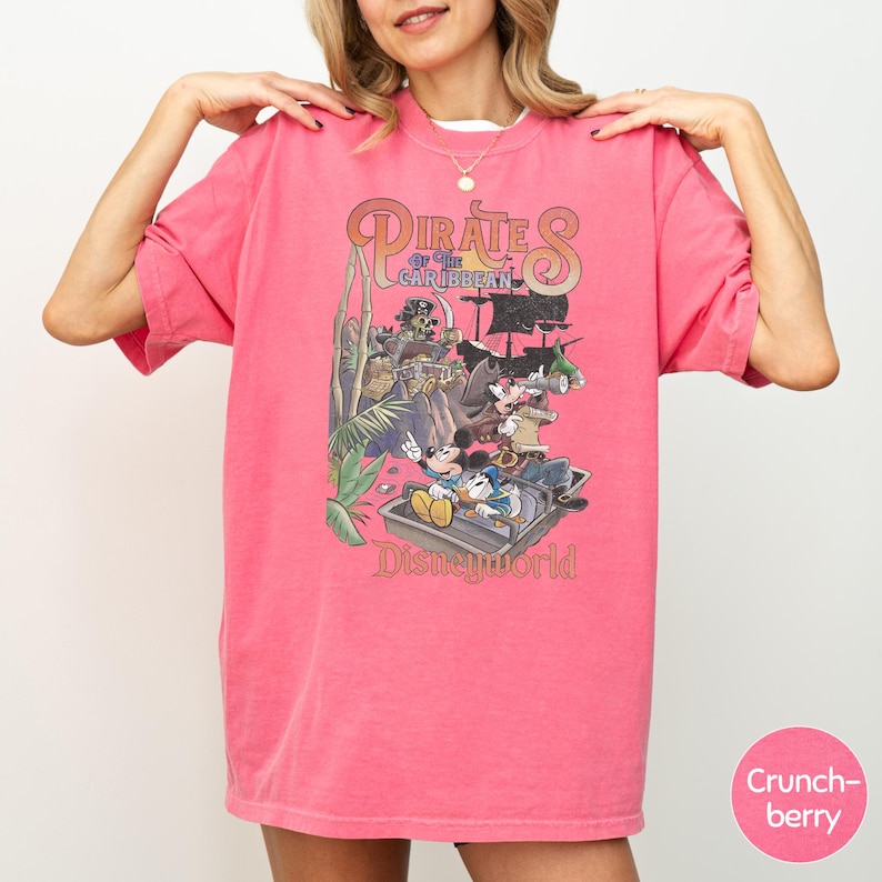 A woman wearing a pink t-shirt with a graphic of Disney characters and text related to the Pirates of the Caribbean ride at Disney World.