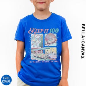 A young boy wearing a blue t-shirt with a graphic design featuring a collage of images related to the Disney theme park, specifically the Space Needle.