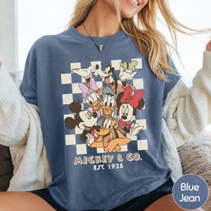 A woman wearing a blue t-shirt with a graphic of Disney characters and text below the image.