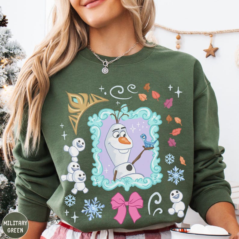 A woman wearing a green sweatshirt with a colorful graphic design featuring characters from the Disney movie Frozen.