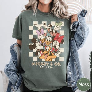 A woman wearing a green t-shirt with a graphic of Disney characters and text below it.