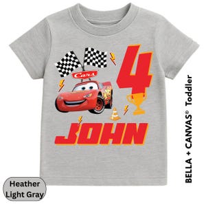 A gray t-shirt with a graphic design featuring a red car and the number 4, along with the text "Cars 4 JOHN".