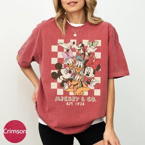 A woman wearing a red t-shirt with a graphic of Disney characters and text.
