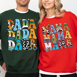 A man and a woman are standing next to each other, both wearing colorful sweatshirts with large, colorful text.