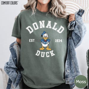 A person wearing a green t-shirt with a graphic of a cartoon duck and the text "DONALD EST. 1934 DUCK" printed on it.