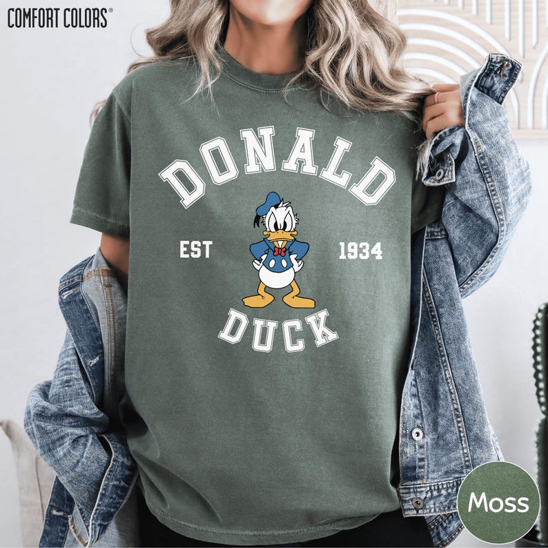 A person wearing a green t-shirt with a graphic of a cartoon duck and the text "DONALD EST. 1934 DUCK" printed on it.