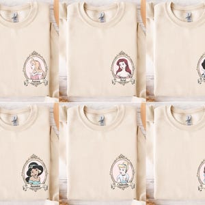 six beige t-shirts with cartoon portraits of princesses and the names "Aria", "Annie", "Annie", "Annie", "Annie", and "Annie" printed on them.