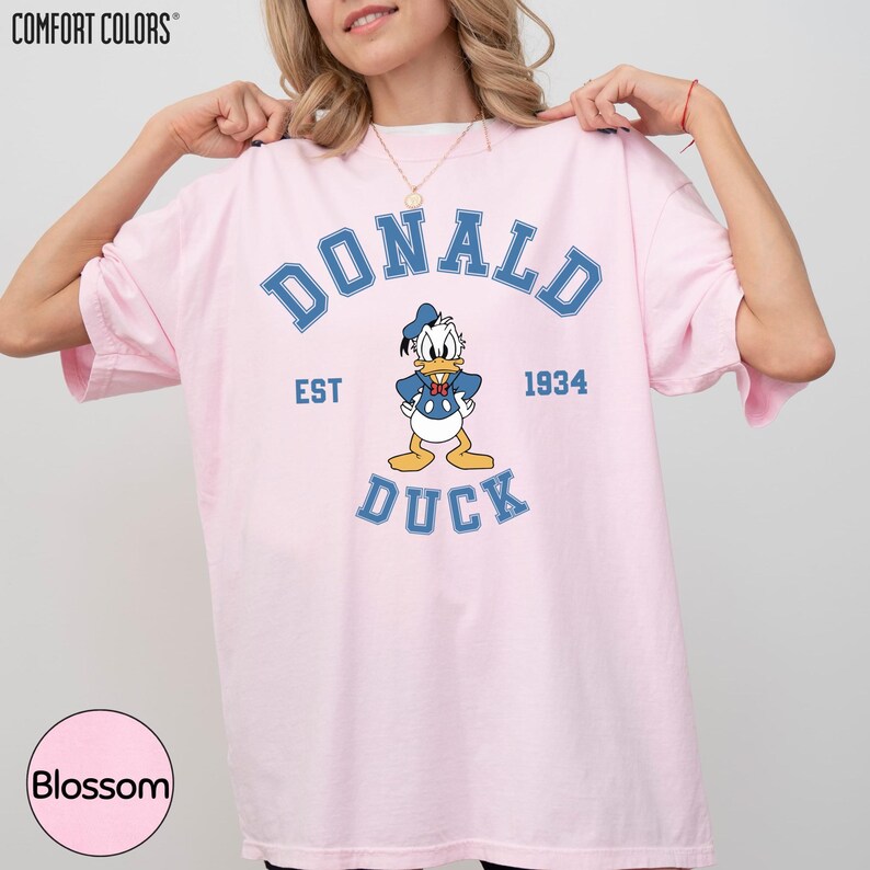 A woman wearing a pink t-shirt with a graphic of a cartoon duck and the text "DONALD DUCK EST 1934" printed on it.