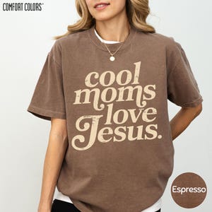 A woman wearing a brown t-shirt with the text "cool moms love Jesus" printed on it.