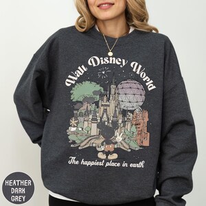 A woman wearing a gray sweatshirt with a graphic design depicting various Disney landmarks and the text "The happiest place in earth".