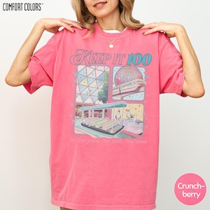 A woman wearing a pink t-shirt with a graphic design of a ferris wheel and other amusement park rides.