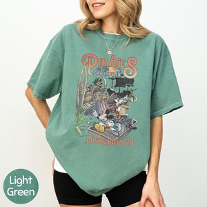 A woman wearing a green t-shirt with a graphic of Disney characters from the Pirates of the Caribbean ride at Disneyworld.