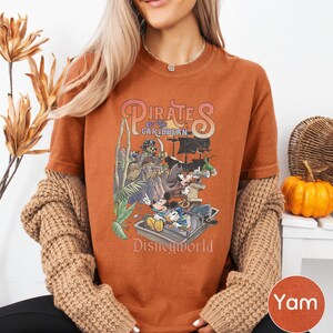 A woman wearing a t-shirt with a Disney Pirates of the Caribbean graphic, sitting in front of a wicker basket and a small pumpkin.