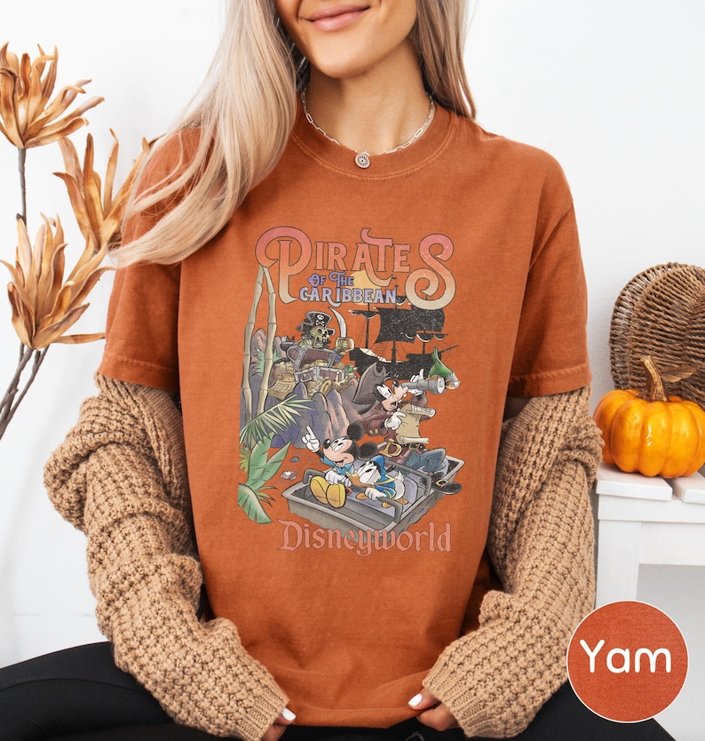 A woman wearing a t-shirt with a Disney Pirates of the Caribbean graphic, sitting in front of a wicker basket and a small pumpkin.