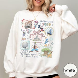 A woman wearing a white sweater with a collage of Disney-themed illustrations and text, including characters like Minnie Mouse, Mickey Mouse, and Goofy, along with various Disney landmarks and elements.