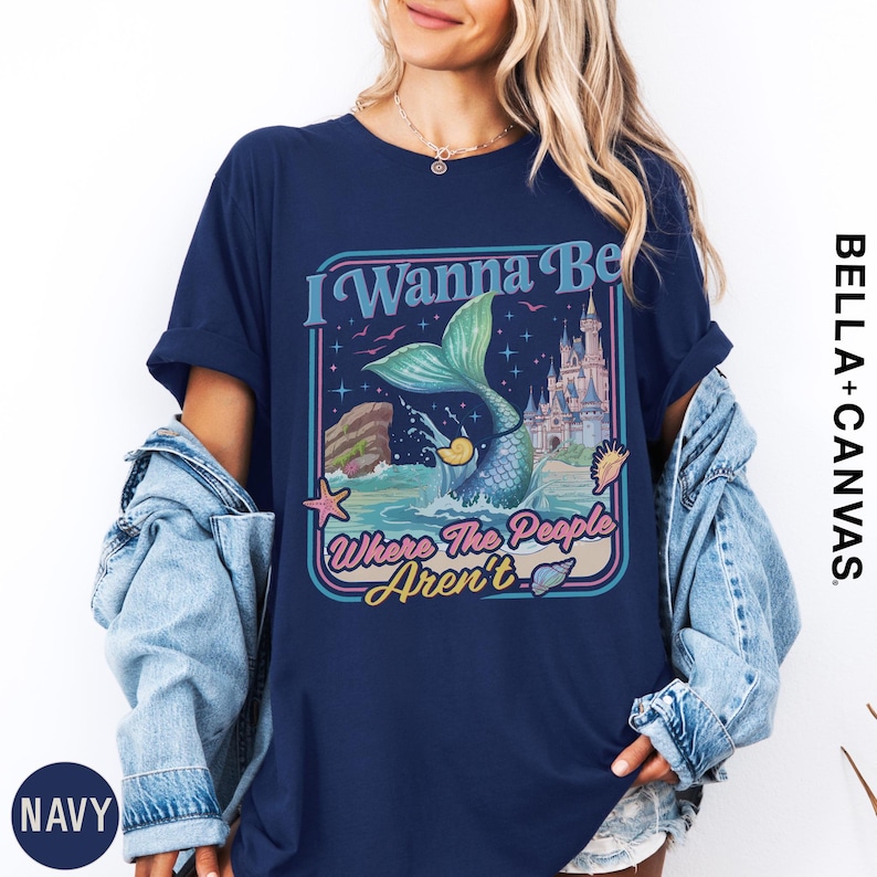 A woman wearing a navy blue t-shirt with a graphic design featuring a mermaid and the text "I Wanna Be Where The People Aren't".
