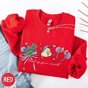 A red sweater with a cartoon fish design and the text "Part of your world" printed on it, along with a necklace and some other clothing items.