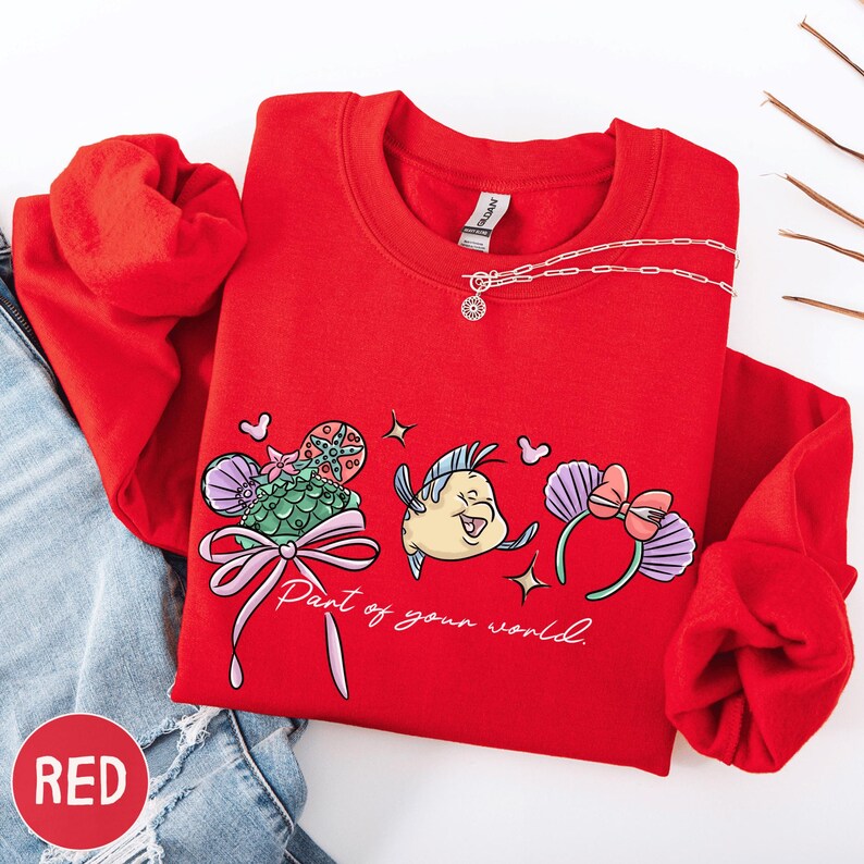 A red sweater with a cartoon fish design and the text "Part of your world" printed on it, along with a necklace and some other clothing items.