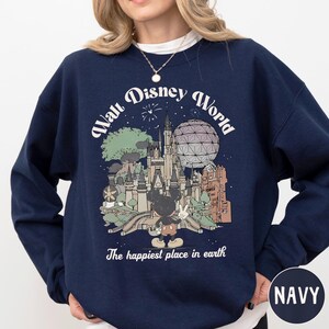A navy blue sweatshirt with a graphic design depicting a Disney theme park, including Mickey Mouse and various Disney landmarks.