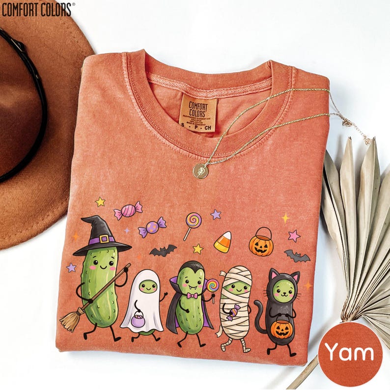 a t-shirt with a Halloween-themed design, including a group of cartoon vegetables dressed in costumes and surrounded by Halloween-related elements such as bats, pumpkins, and candy canes.