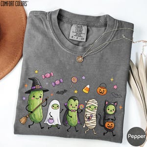 A gray t-shirt with a Halloween-themed design featuring a group of cartoon characters dressed in costumes, including a witch, pumpkin, ghost, and mummy.