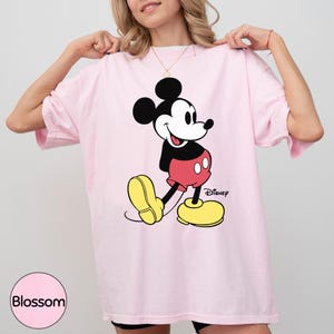 A woman wearing a pink t-shirt with a Mickey Mouse graphic on it.
