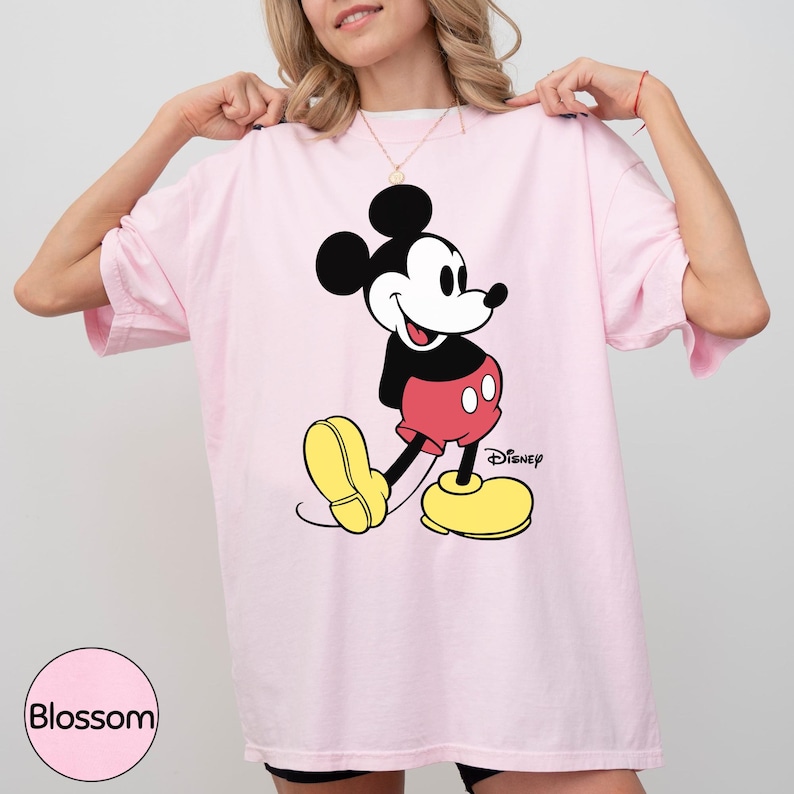 A woman wearing a pink t-shirt with a Mickey Mouse graphic on it.