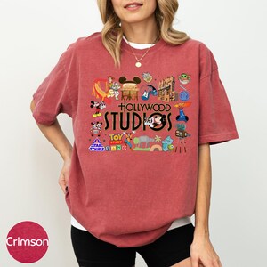 A woman wearing a red t-shirt with various Disney and Pixar-themed graphics and text, including characters, logos, and iconic landmarks.