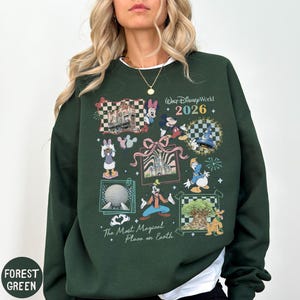A woman wearing a green sweatshirt with various Disney characters and landmarks printed on it, including Mickey Mouse, Minnie Mouse, Goofy, and the Eiffel Tower.