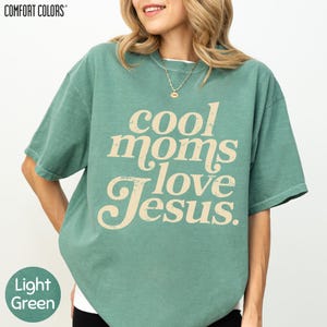 A woman wearing a green t-shirt with the text "cool moms love Jesus" printed on it.