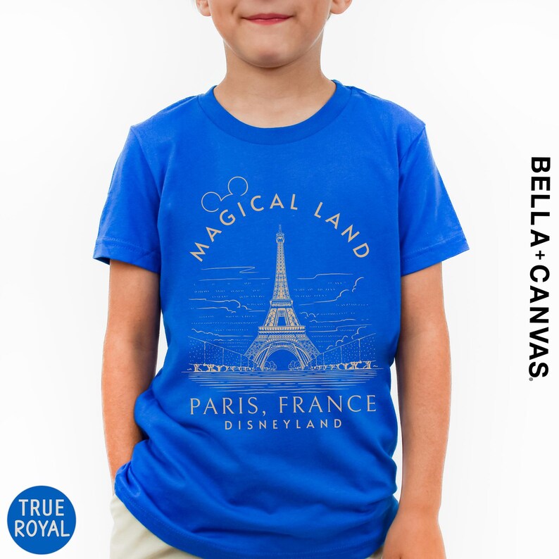 A young boy wearing a blue t-shirt with a graphic design of the Eiffel Tower and text that says "Magical Land Paris, France Disneyland".