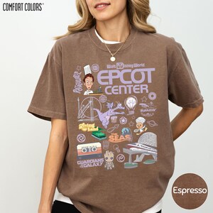 A woman wearing a brown t-shirt with various Disney-themed graphics and text, including a chef, a roller coaster, and other iconic landmarks and characters.