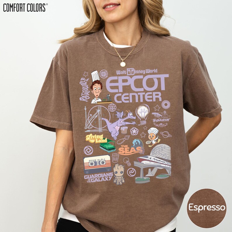 A woman wearing a brown t-shirt with various Disney-themed graphics and text, including a chef, a roller coaster, and other iconic landmarks and characters.