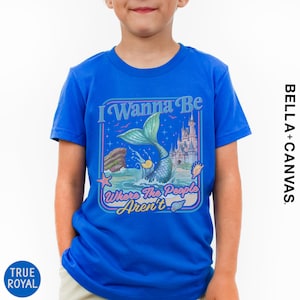 A young boy wearing a blue t-shirt with a colorful graphic design featuring a mermaid, castle, and text.