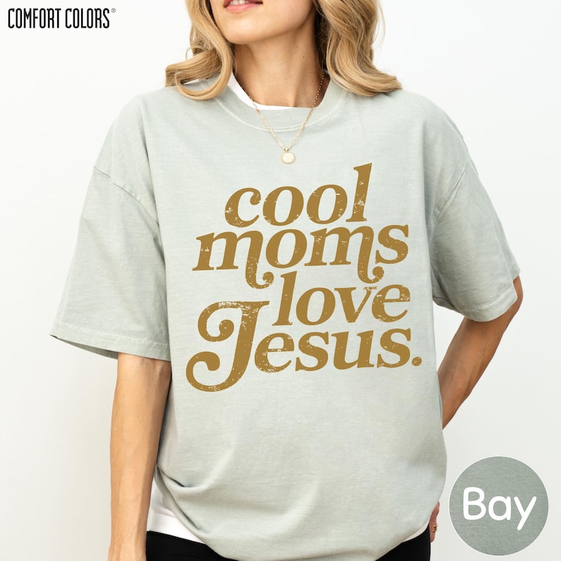 A woman wearing a gray t-shirt with the text "cool moms love Jesus" printed on it.