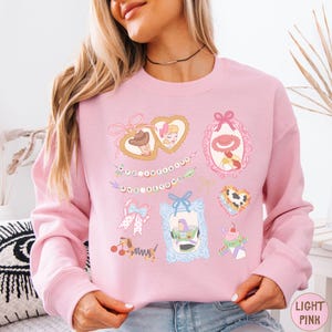A woman wearing a pink sweatshirt with various cartoon-style illustrations and text on it.