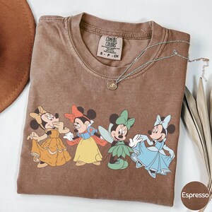 A brown t-shirt with a cartoon image of Minnie Mouse and Snow White, along with a necklace and a brown hat.