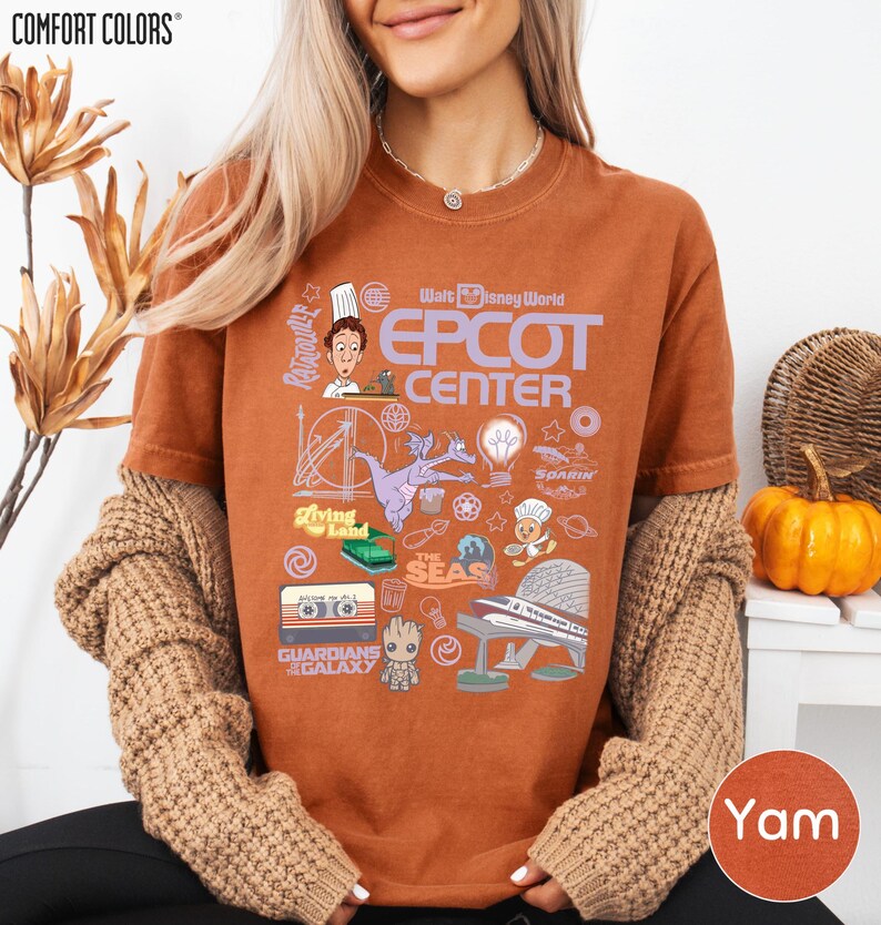 A woman wearing a brown sweater and a t-shirt with various Disney-themed graphics and text, including a chef, roller coaster, and other iconic elements.