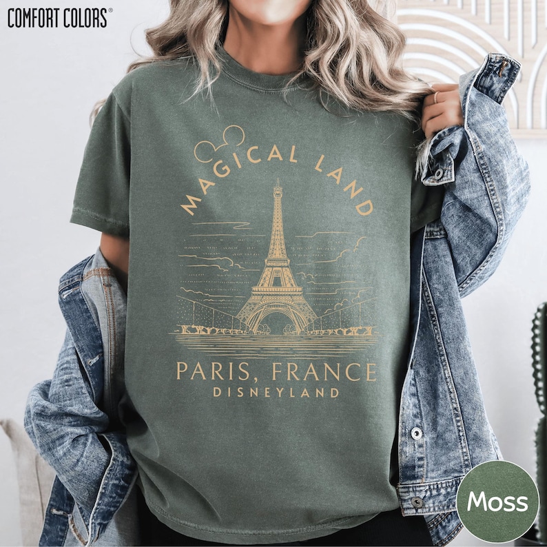 A person wearing a green t-shirt with a graphic design of the Eiffel Tower and text that says "Magical Land Paris, France Disneyland".