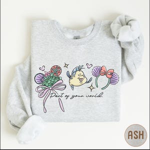 A gray sweatshirt with a colorful graphic design featuring a cartoon fish, flowers, and a ribbon. The text on the sweatshirt says "Part of your world."