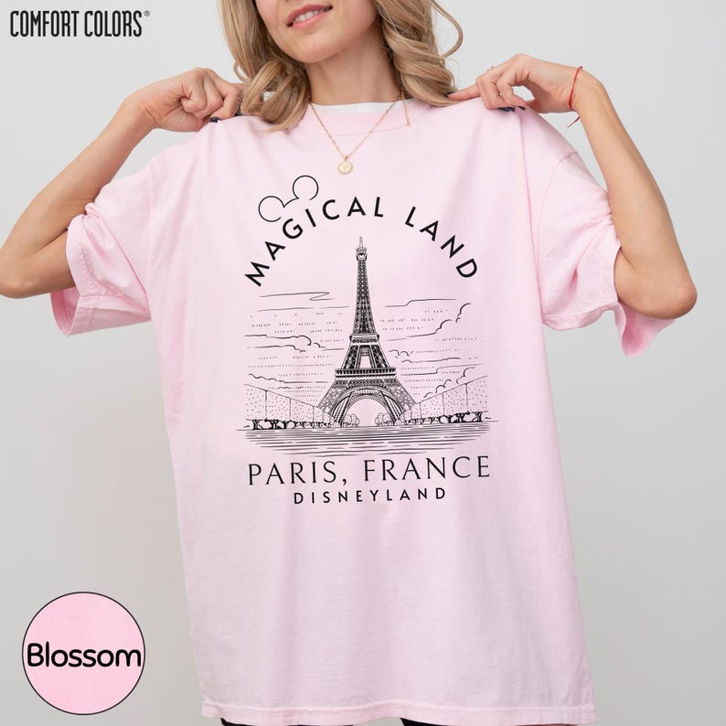 A woman wearing a pink t-shirt with a graphic of the Eiffel Tower and the text "Magical Land Paris, France Disneyland" printed on it.