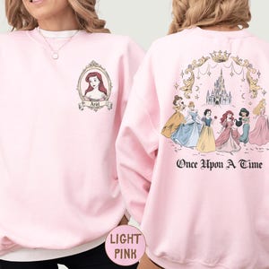 A woman wearing a pink sweatshirt with a design featuring Disney princesses and the text "Once Upon a Time" on the back.