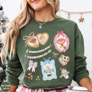 A woman wearing a green sweatshirt with various cartoon-style illustrations and text on it.