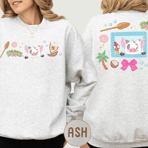 A woman wearing a gray sweatshirt with a cartoon pig design and various tropical elements on the back.