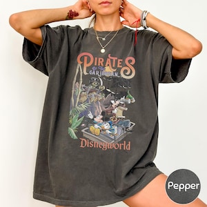 A person wearing a black t-shirt with a graphic of Disney characters and the text "PIRATES OF THE CARIBBEAN" printed on it.