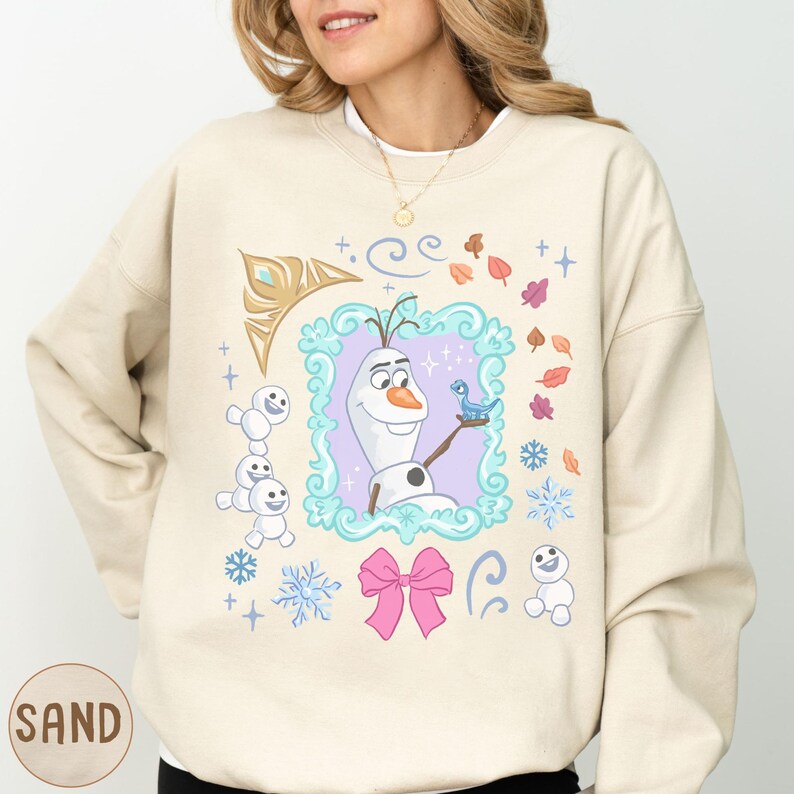 A woman wearing a beige sweater with a colorful graphic design featuring characters from the Disney movie Frozen.
