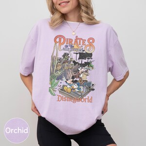A woman wearing a purple t-shirt with a graphic design of Disney characters from the Pirates of the Caribbean ride at Disneyworld.