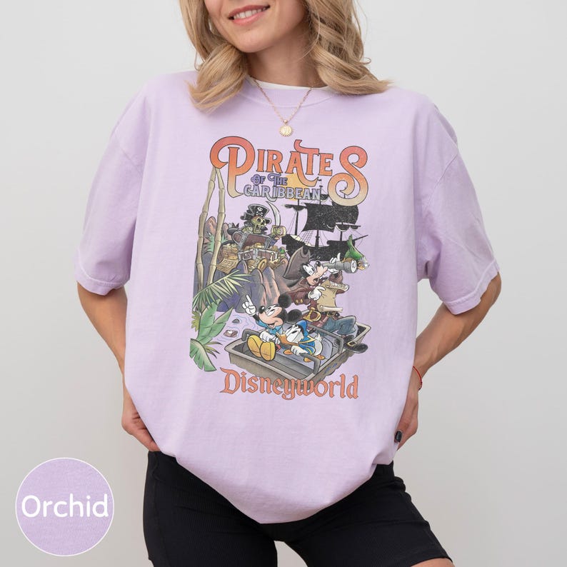 A woman wearing a purple t-shirt with a graphic design of Disney characters from the Pirates of the Caribbean ride at Disneyworld.