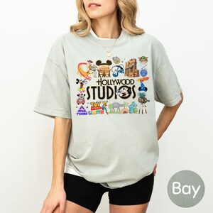 A woman wearing a grey t-shirt with various Disney and Hollywood Studios logos and characters printed on it.